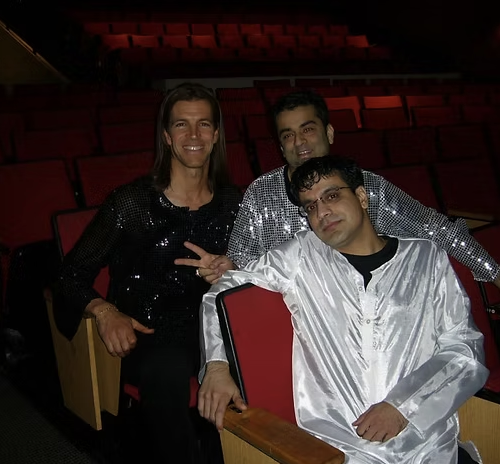 Rajeev Pahuja in a white kurta posing with two performers among auditorium seats